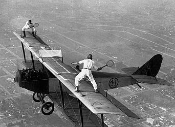 Daredevils playing tennis on a biplane.